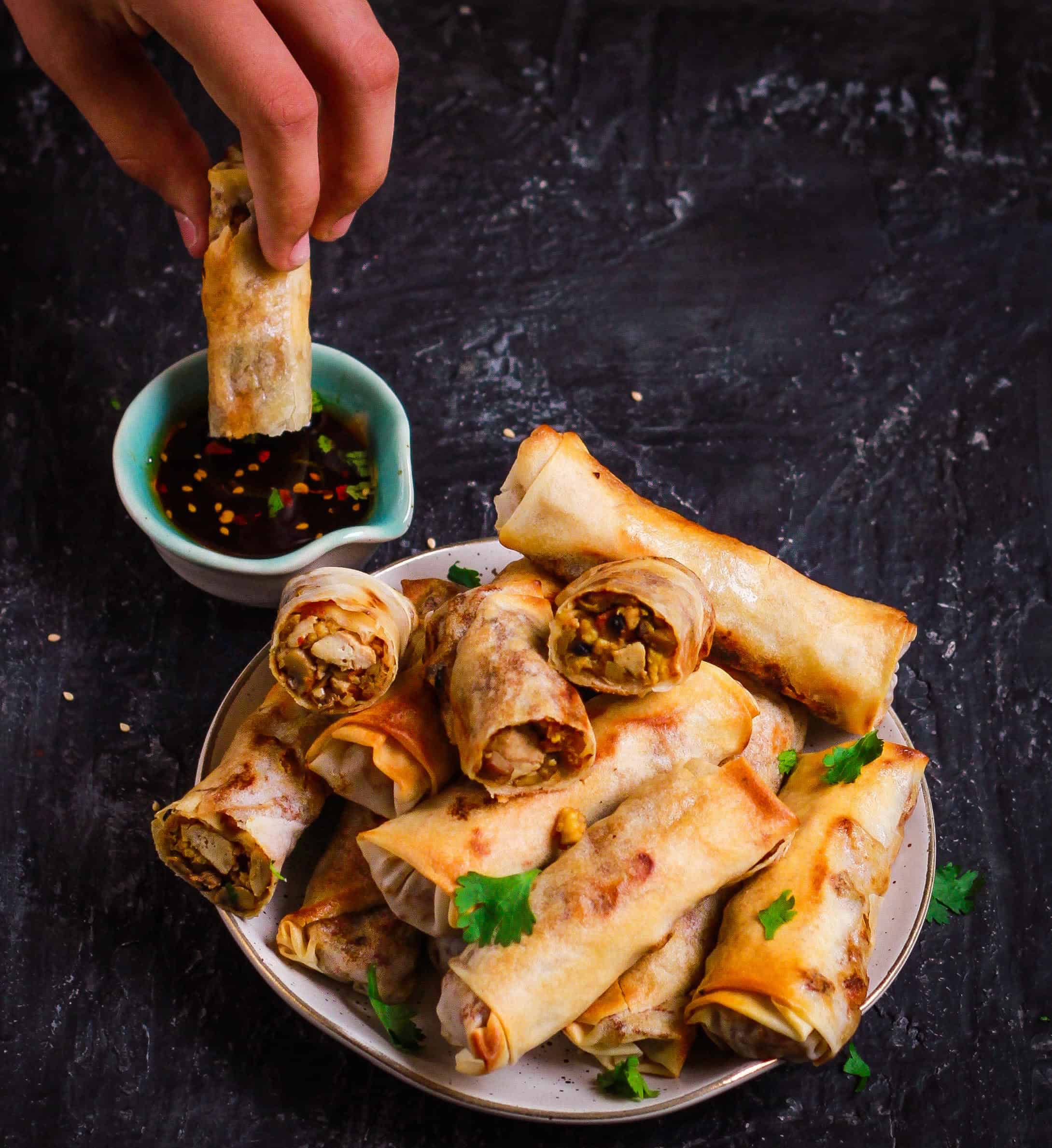 A platter of spring rolls with one getting dipped in a dipping sauce.