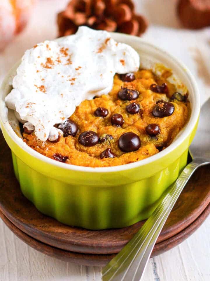 pumpkin mug cake with chocolate chips and whipped cream on a plate.