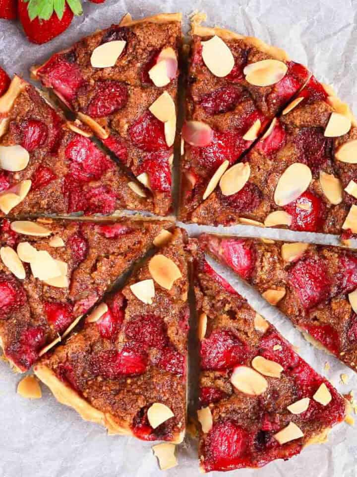 A sliced tart with almonds and strawberries on parchment paper.