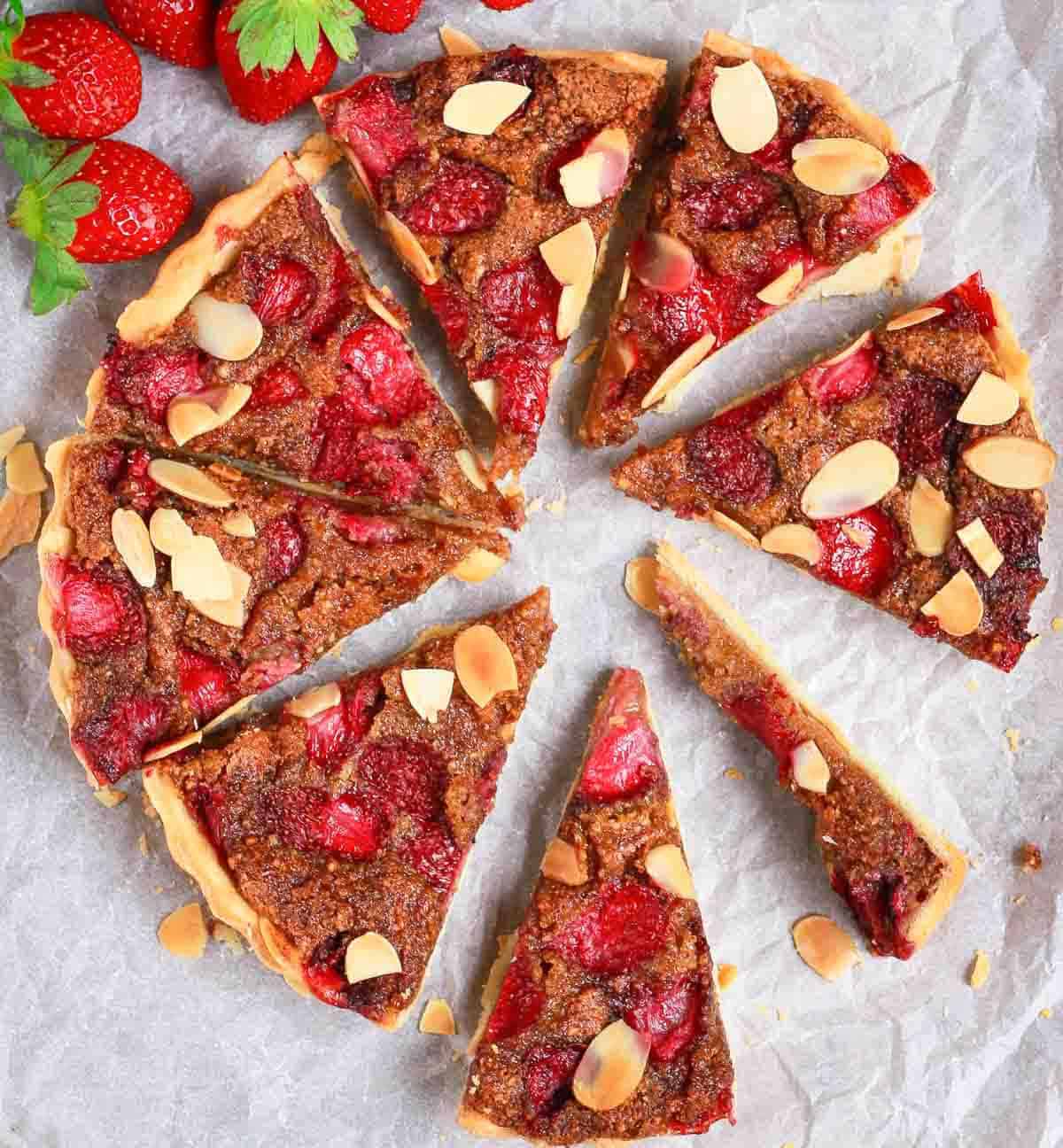 Sliced pie with strawberries and almonds on a white paper.