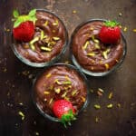 3 bowls of chocolate pudding garnished with strawberries and pistachios.