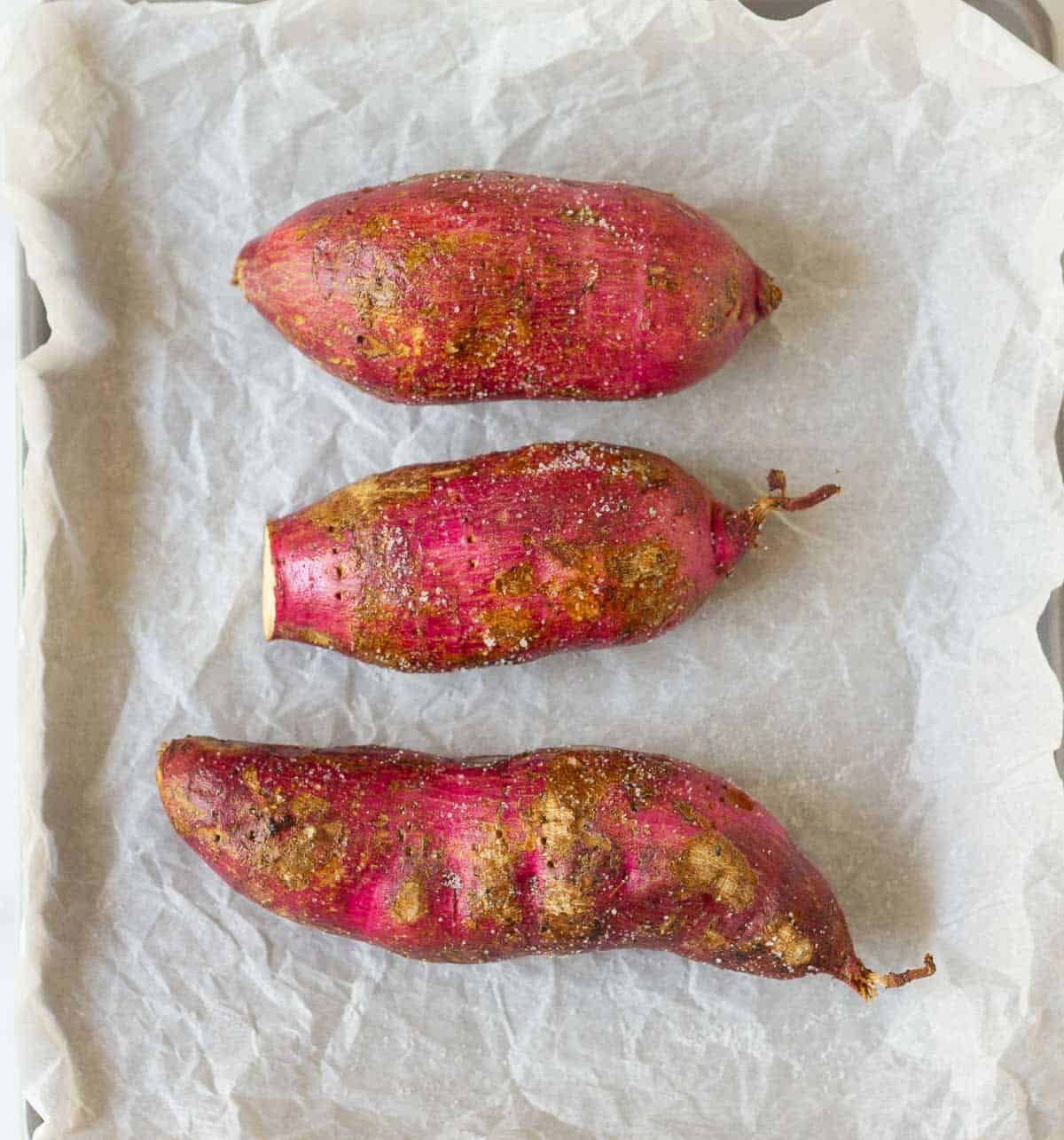 3 sweet potatoes coated with oil and salt on parchment paper.