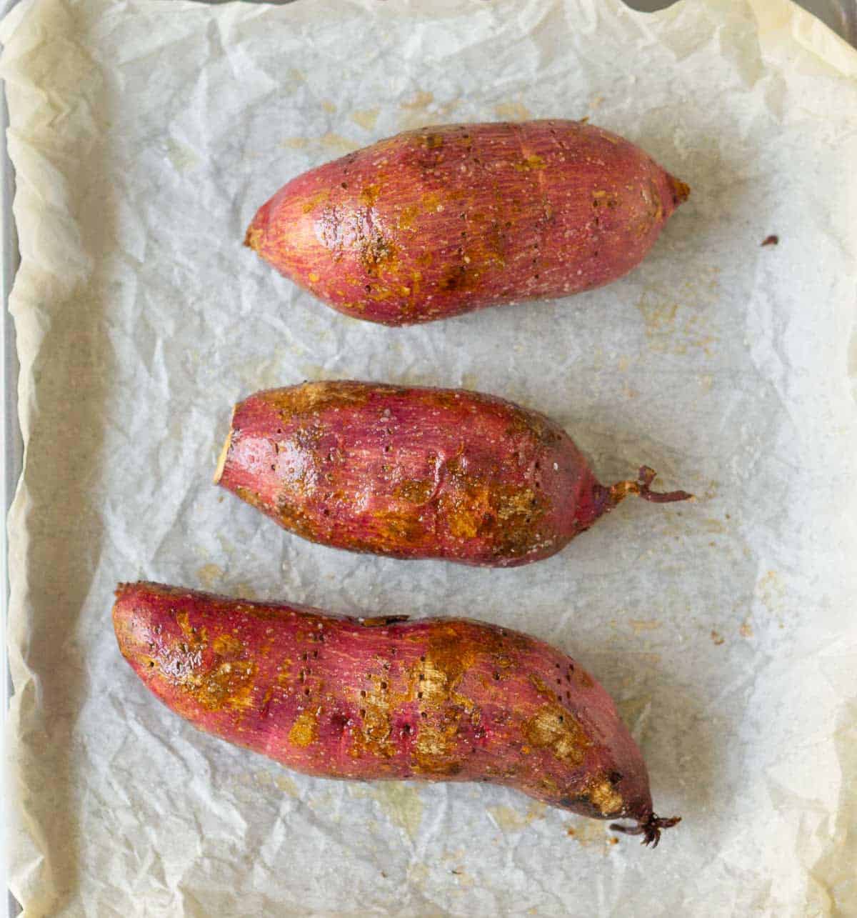3 baked sweet potatoes on parchment paper.