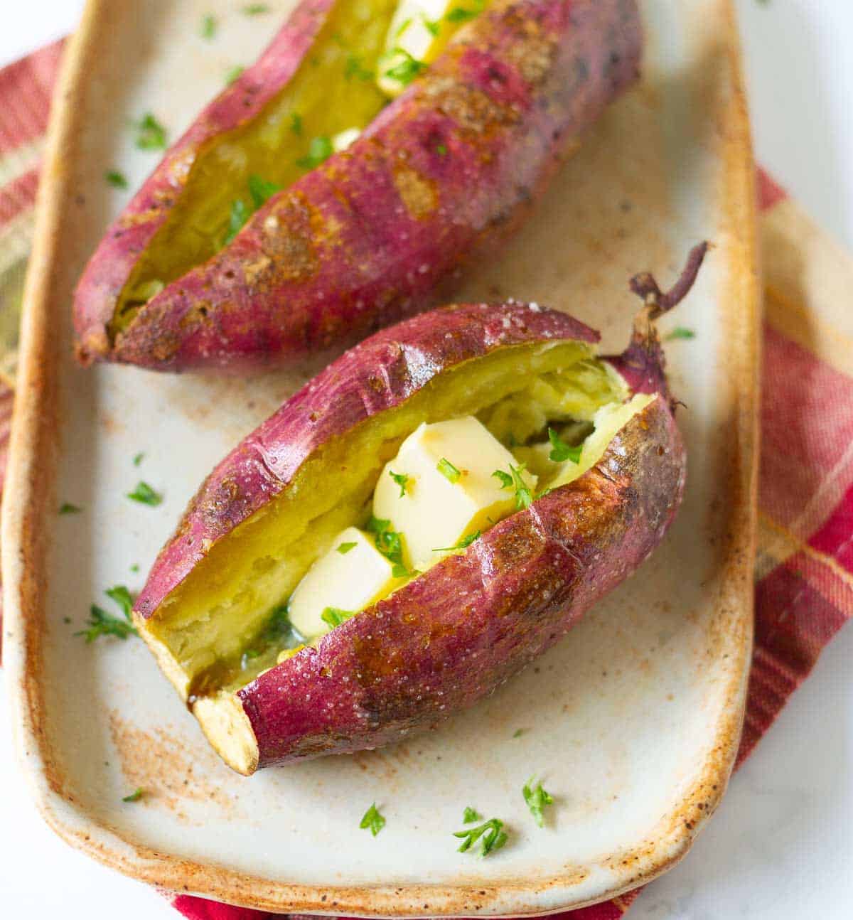 2 sweet potatoes topped with butter and parsley on a platter.