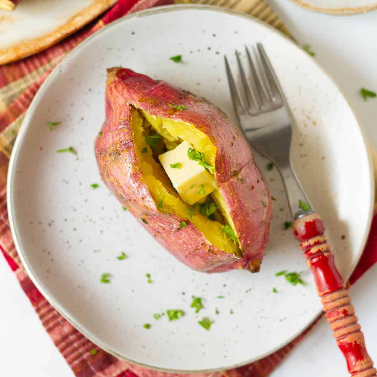 Sweet potato with butter and parsley on a plate with a red fork.