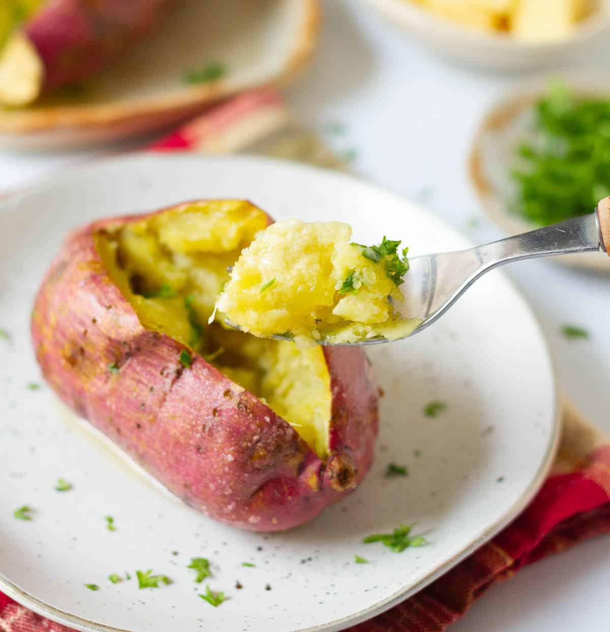 A bite of cooked sweet potato on a fork on top of a plate.
