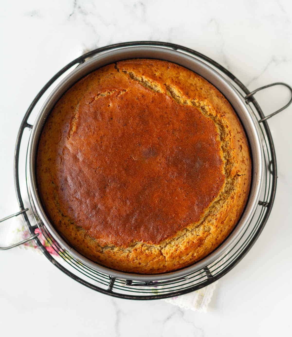 Baked cake in a cake pan on a wire rack.