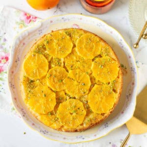 Upside down orange cake with pistachios on a cake platter.