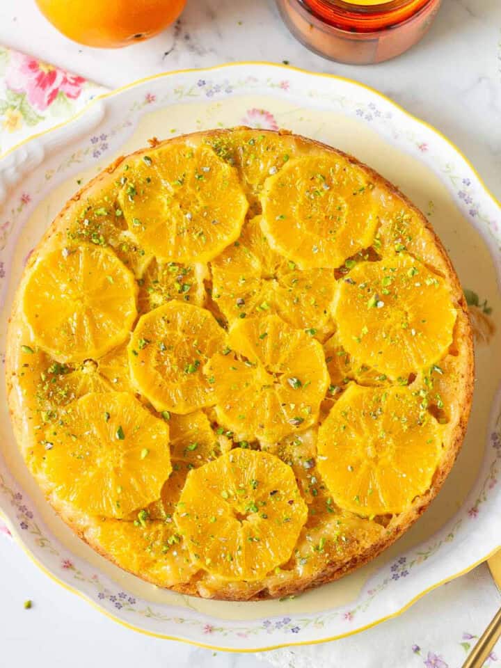 Upside down orange cake with pistachios on a cake platter.