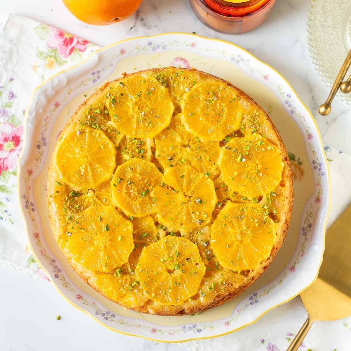 Upside down orange cake with pistachios on a cake platter.