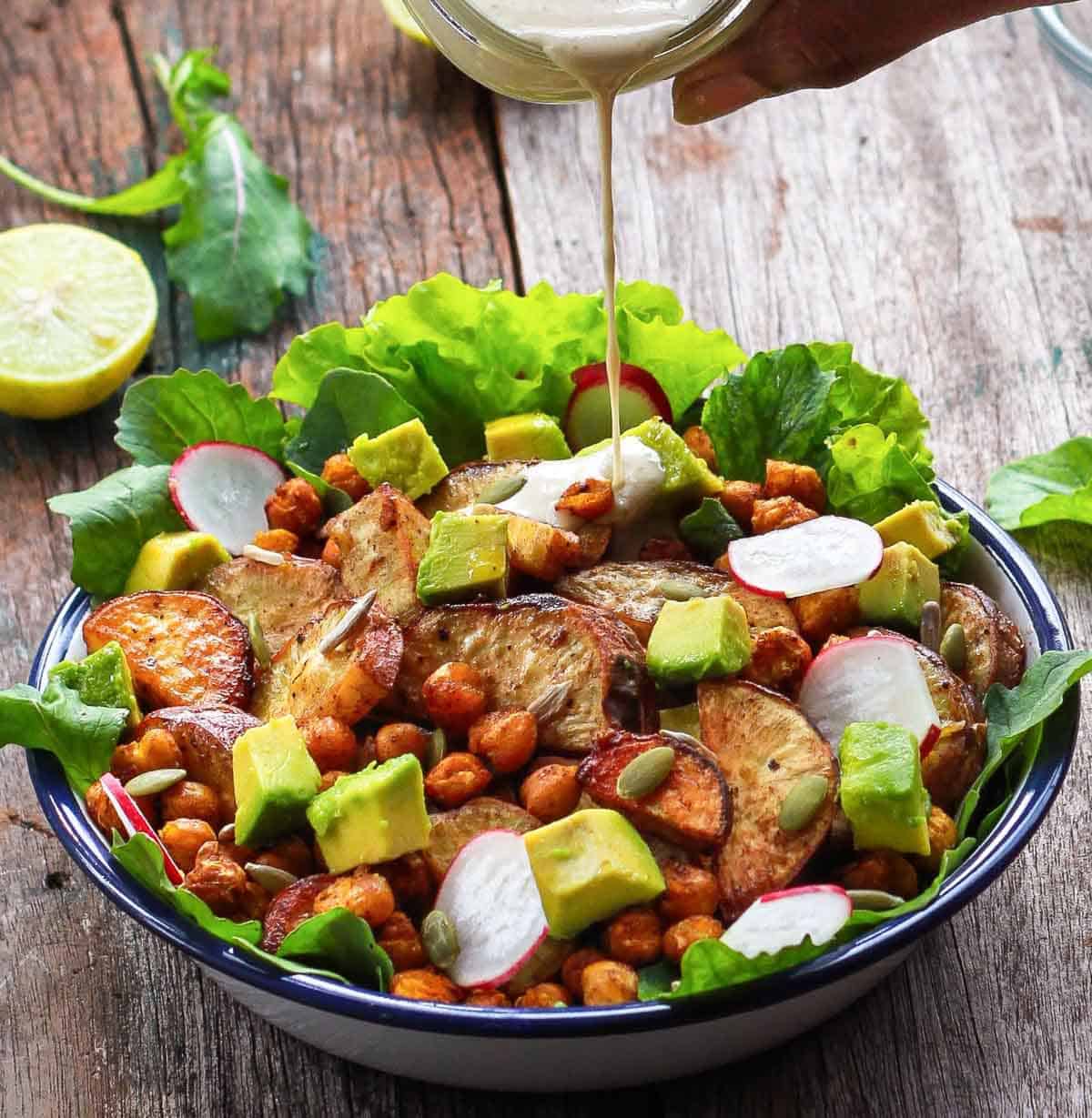 A hand pouring dressing on a salad from a jar.