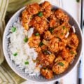 A bowl of sticky sesame cauliflower and rice with chopsticks on the side.