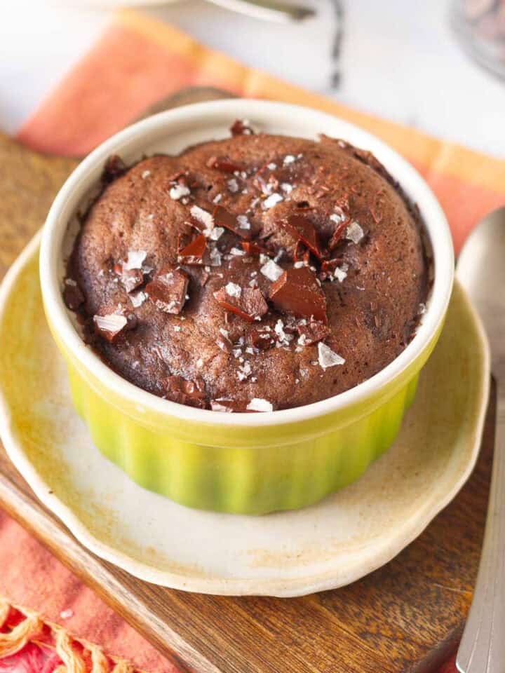 brownie mug cake in a green ramekin on a small plate and wooden board.