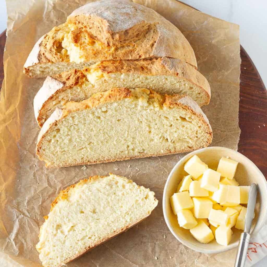 Sliced bread on a board with cubed butter in a bowl with a butter knife.