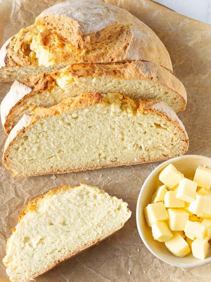 Sliced bread on a board with cubed butter in a bowl with a butter knife.