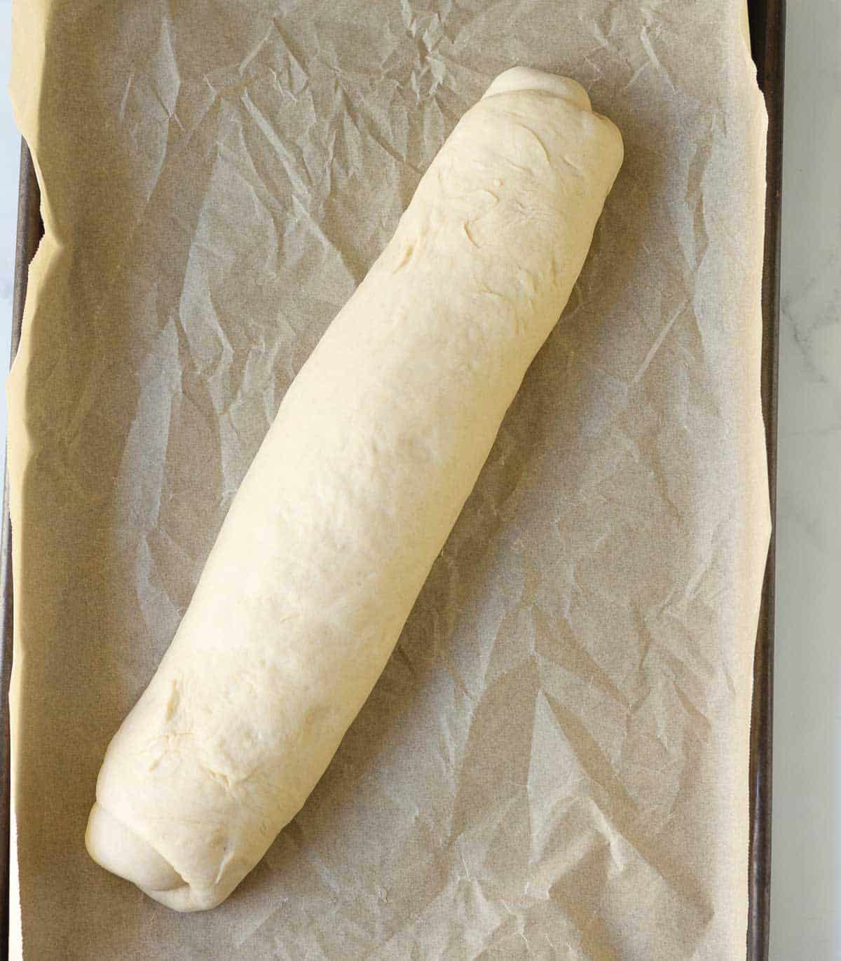 Bread dough in a baguette shape on a parchment-lined tray.