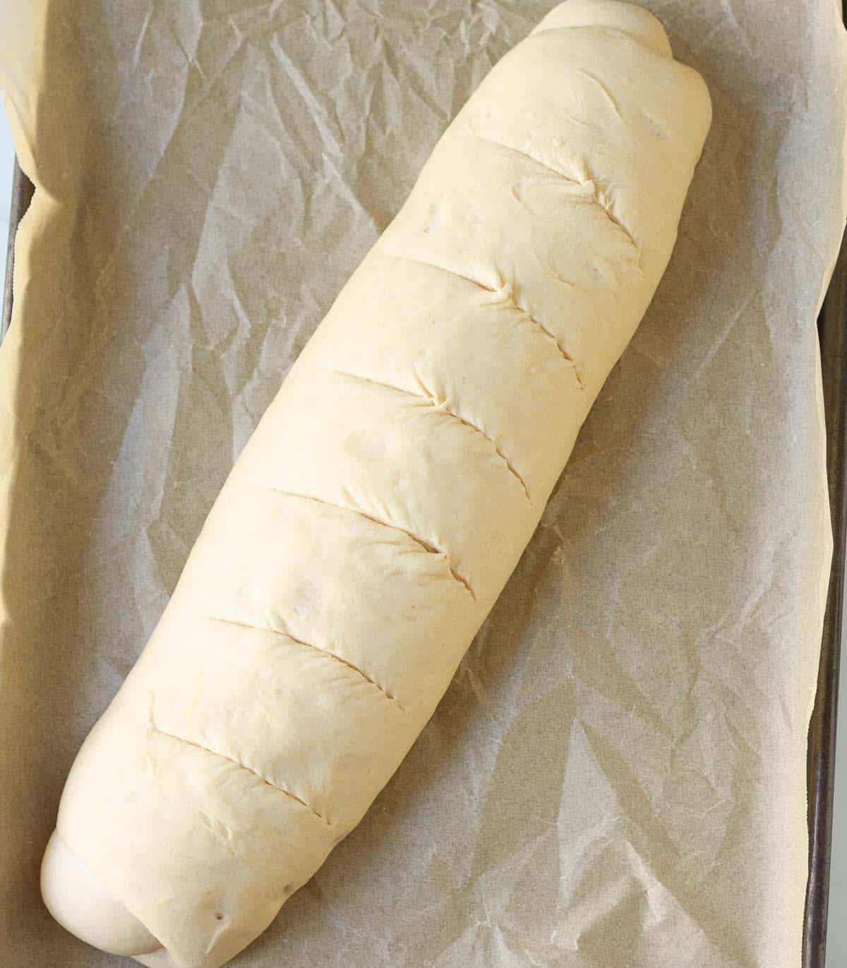 Scored baguette shaped bread dough on a tray.
