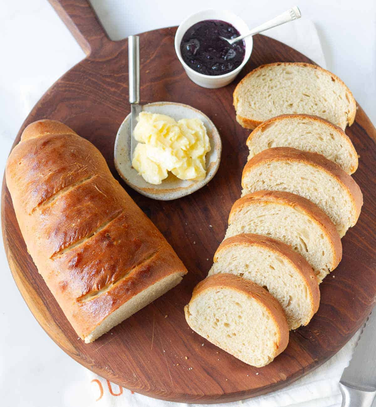 Half a loaf of bread and sliced bread with butter and jam on a board.