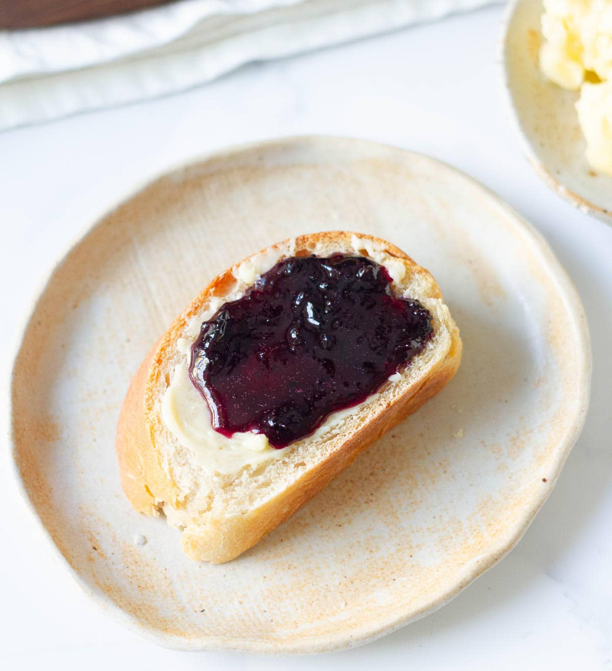 A slice of bread with butter and jam on a small plate.
