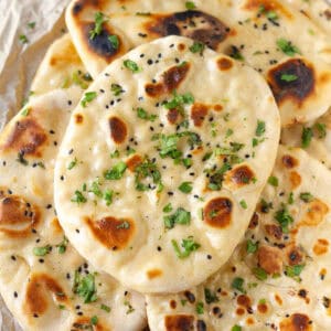A stack of naan breads topped with onion seeds and cilantro.