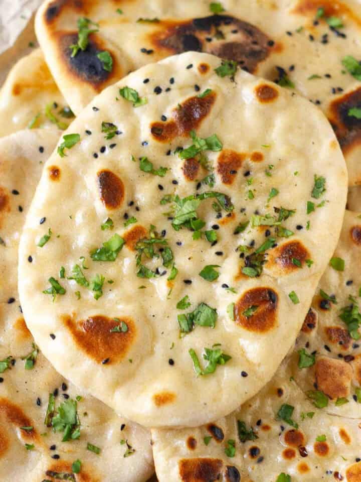 A stack of naan breads topped with onion seeds and cilantro.