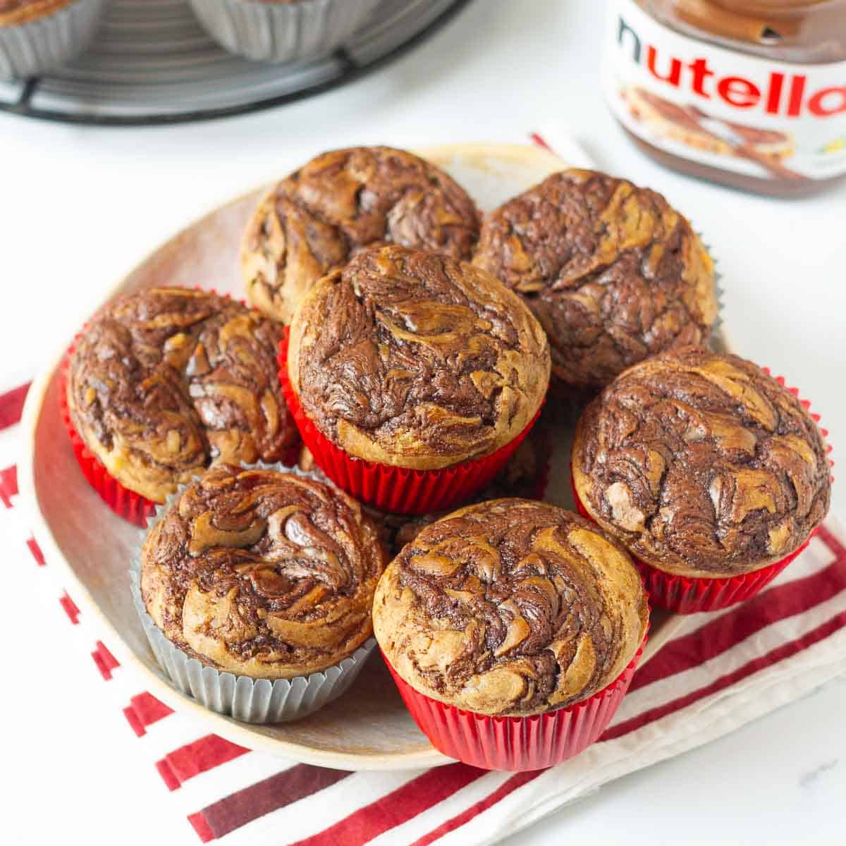 A plate stacked with nutella swirl muffins with a jar of nutella around.