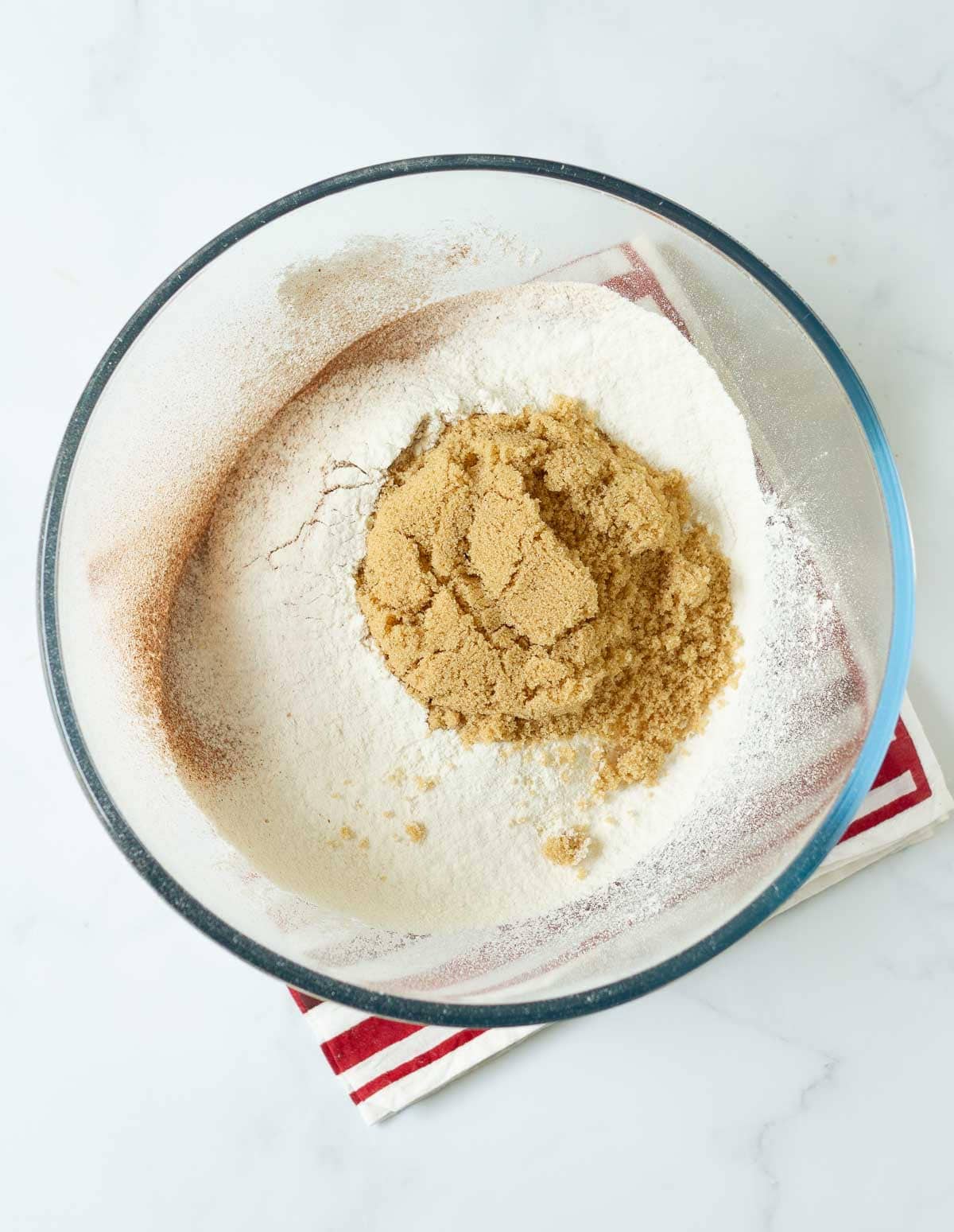 Flour, cinnamon powder, and brown sugar in a glass mixing bowl.