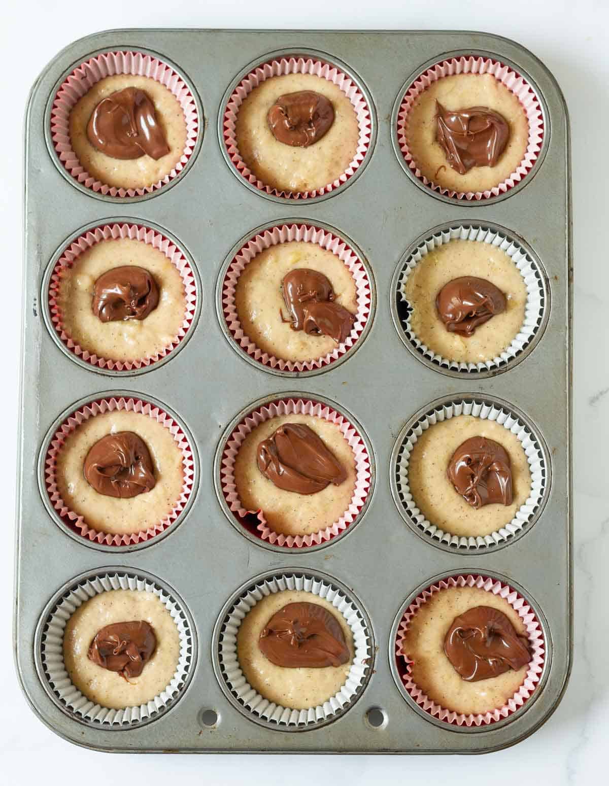Batter in a muffin tray with Nutella on top.