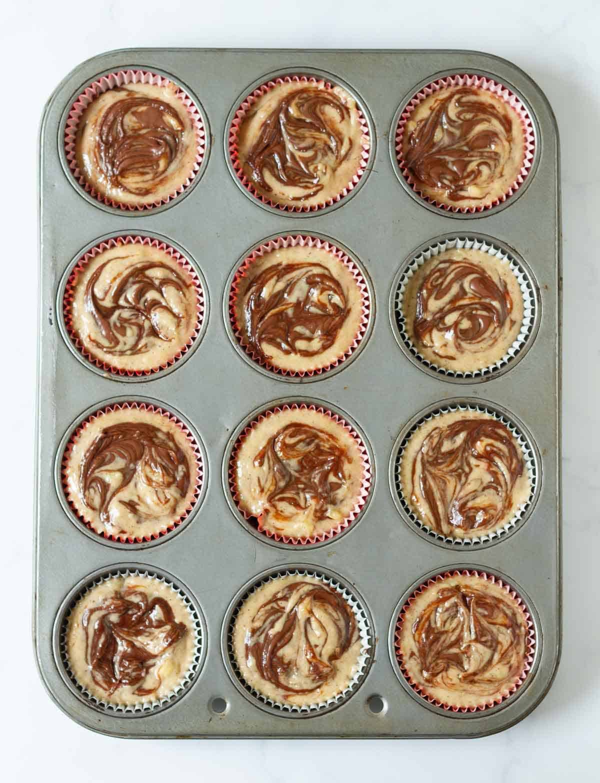 Muffin batter with Nutella swirls in a muffin tray.