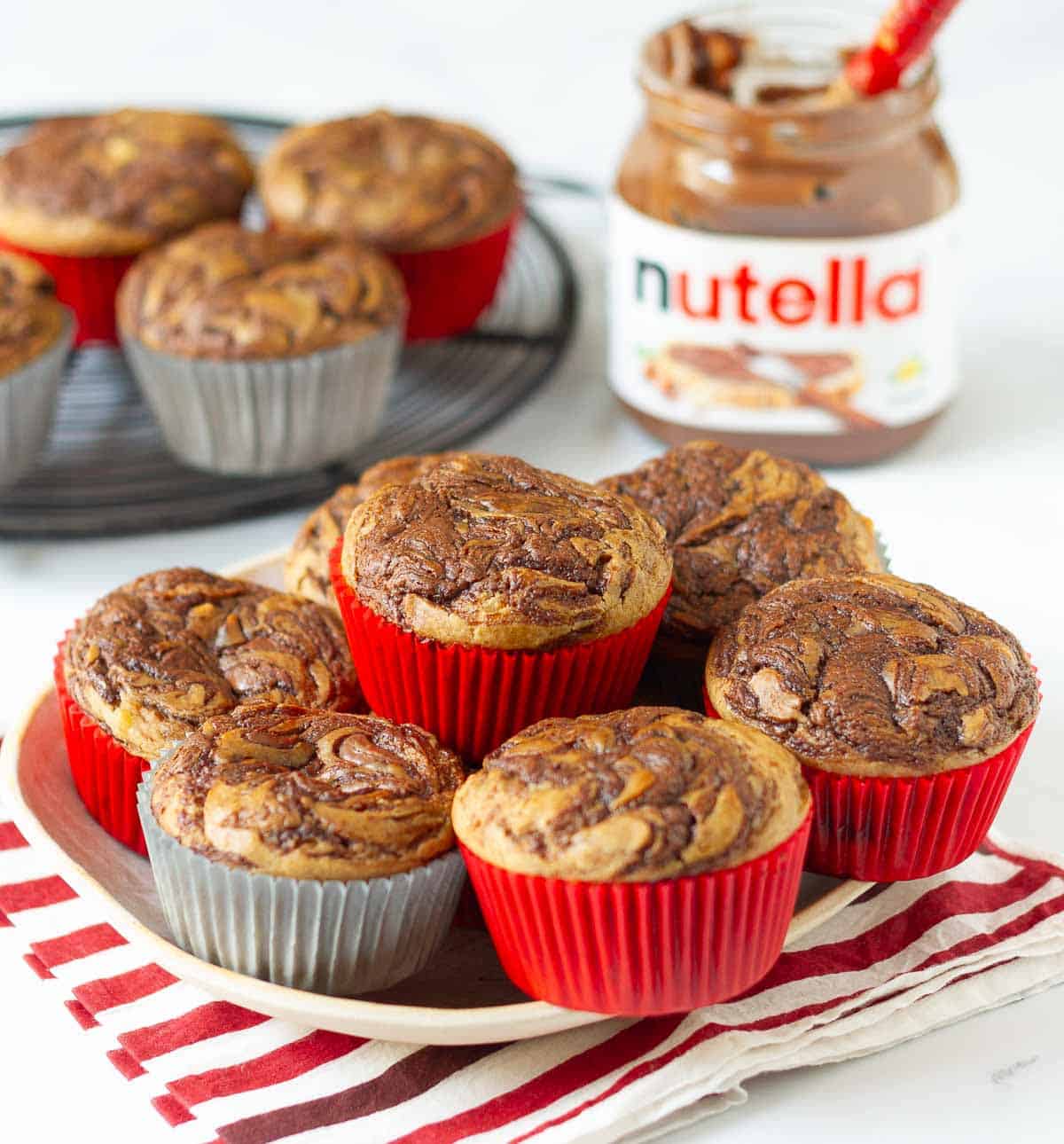 A plate and wire rack with muffins with a jar of Nutella in the background.