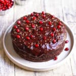 chocolate cake with chocolate frosting and pomegranate arils on top on a platter.