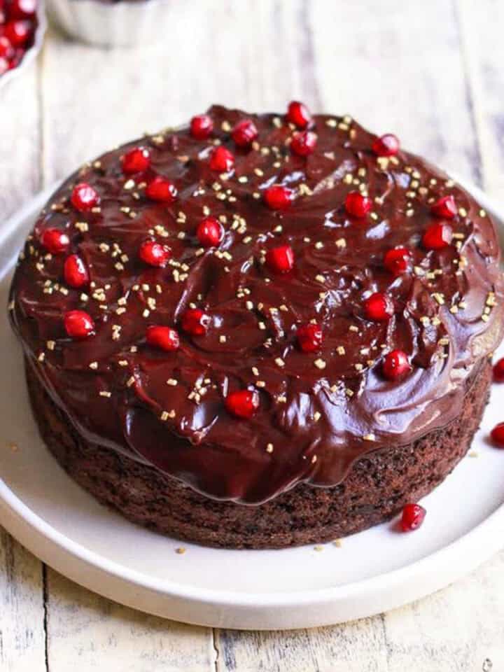 chocolate cake with chocolate frosting and pomegranate arils on top on a platter.