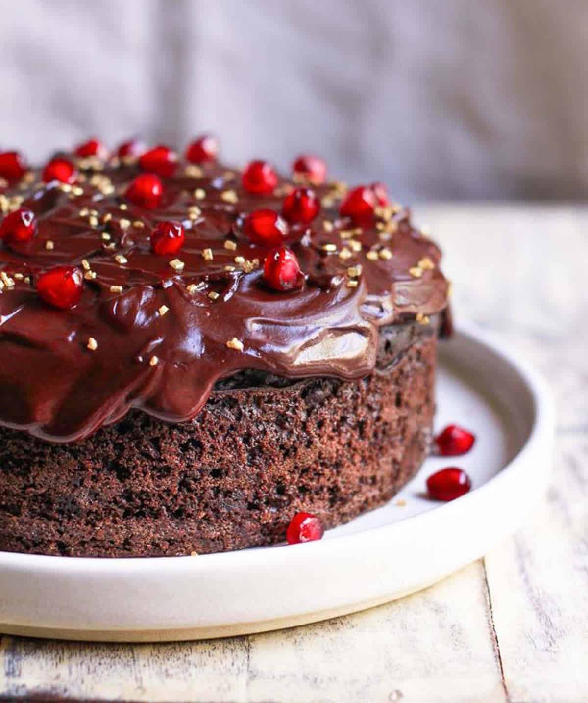 Chocolate cake with ganache and pomegranate arils and sprinkles on a plate.