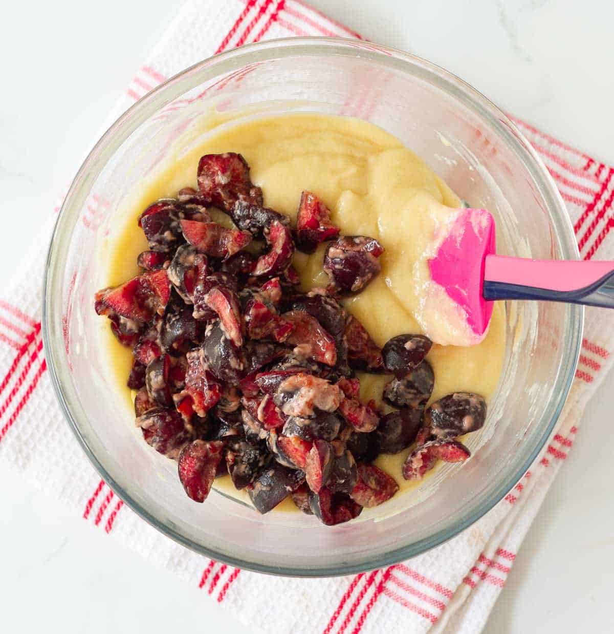 Cherries coated in flour on cake batter in a bowl.