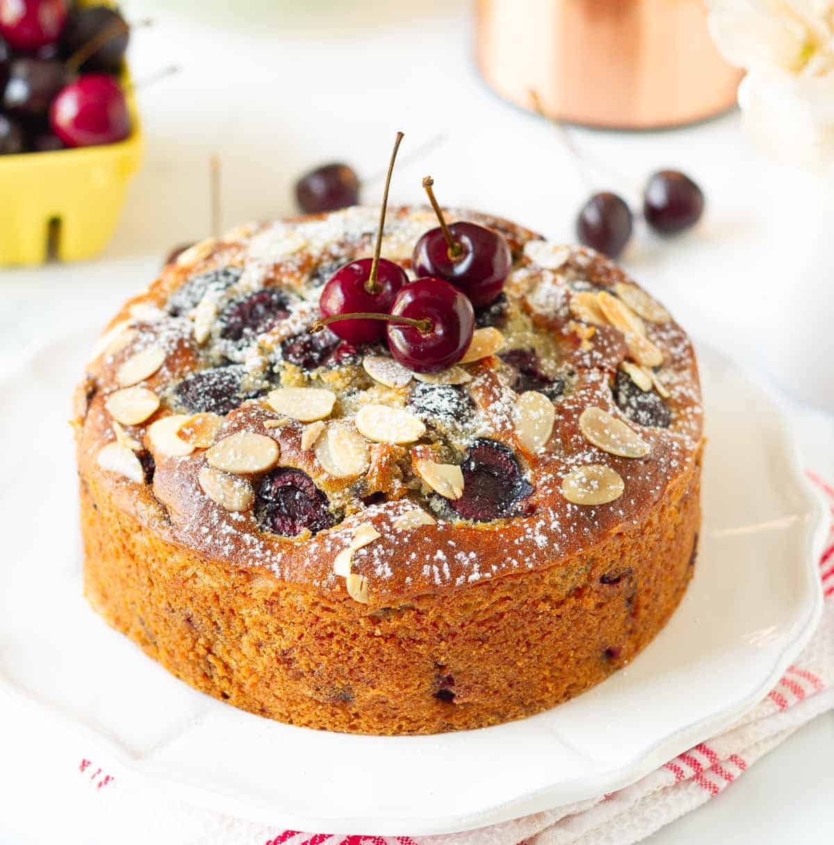 Cherry cake on a white plate with cherries around.