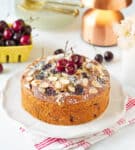 Fresh cherry cake on a plate with cherries and props in the background.
