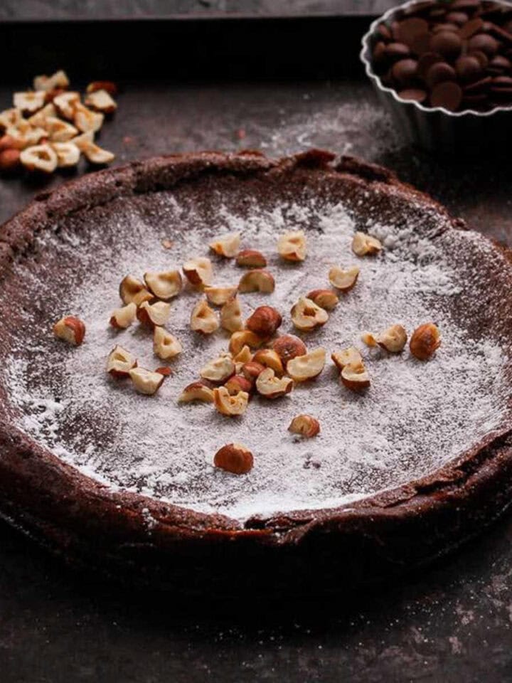 Swedish chocolate cake topped with powdered sugar and hazelnuts on a tray.