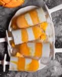 4 mango and coconut layered popsicles on a white tray.