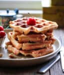 A stack of waffles on a plate with a cherry on top.
