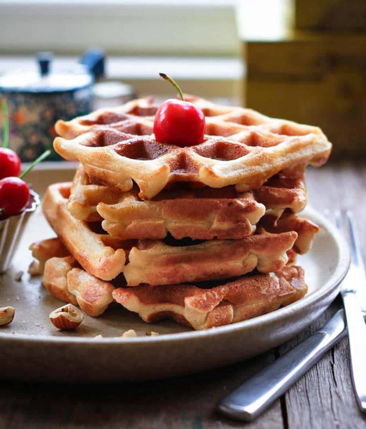 A stack of waffles on a plate with a cherry on top.