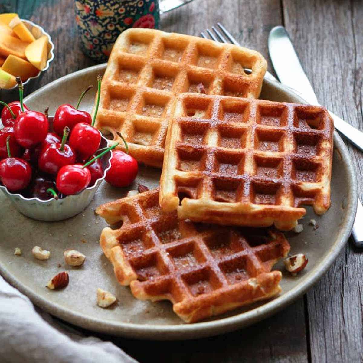 3 waffles on a plate, with cherries and peaches on the side.