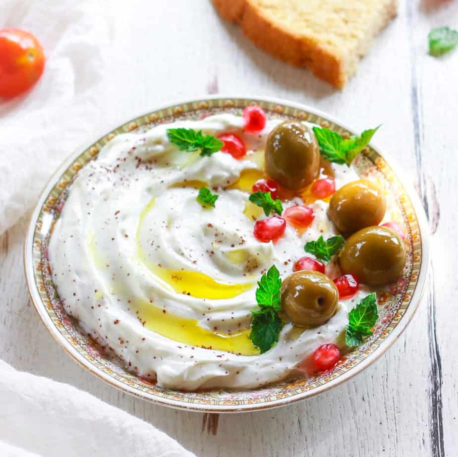 Labneh on a plate topped with olives, pomegranate, sumac, mint and olive oil.