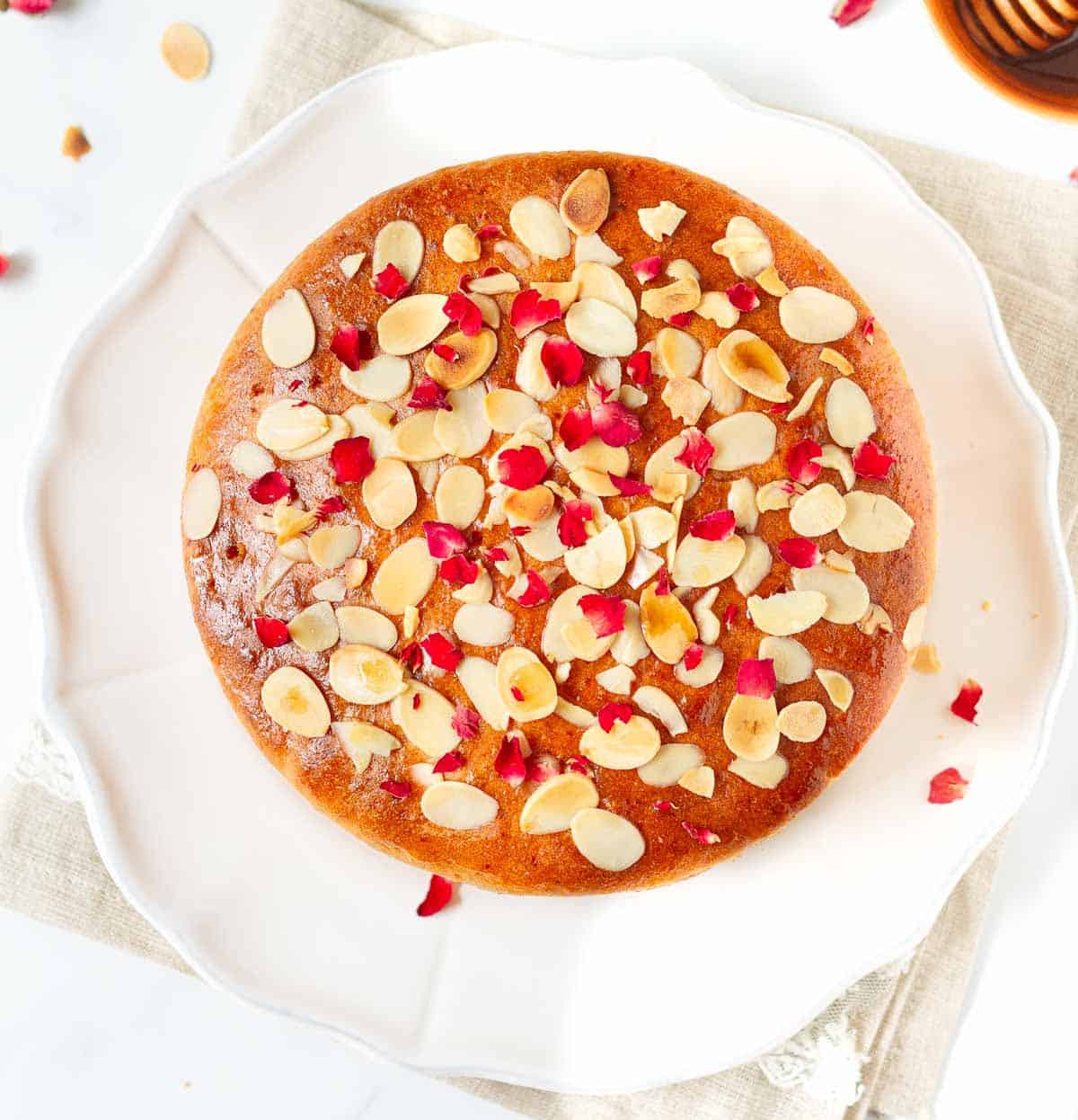 Cake with almond flakes and dried rose petals on a platter.