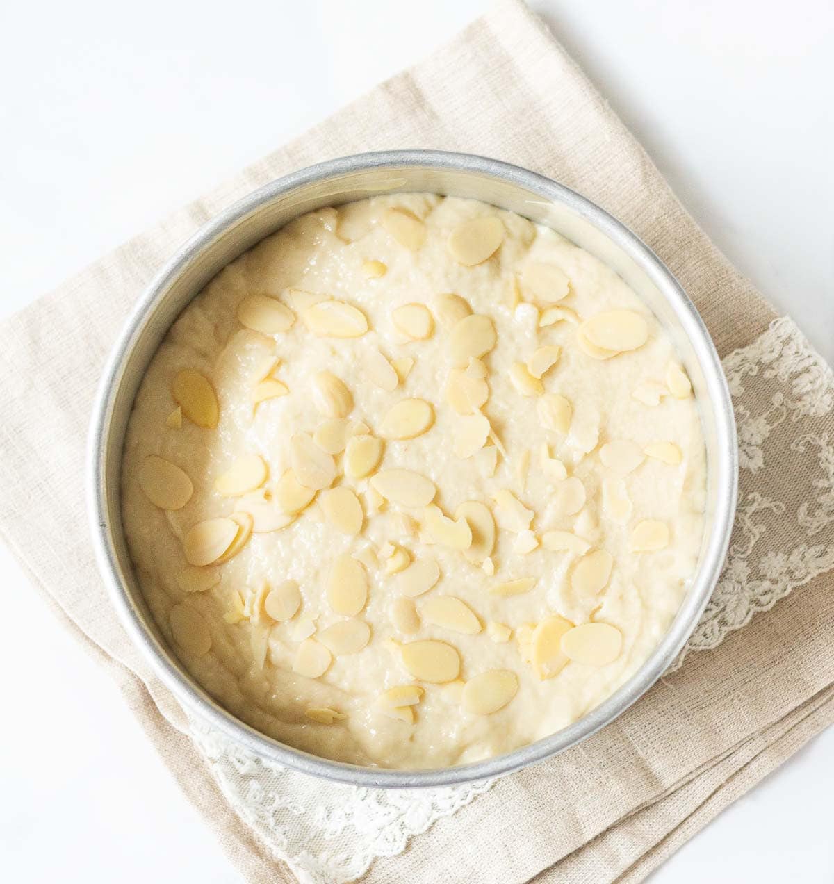 Cake batter in a cake pan with almond flakes on top.