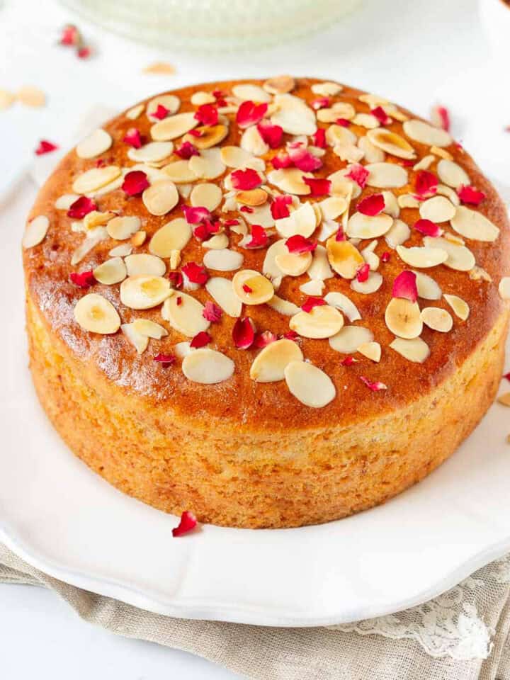 Almond honey cake with rose petals and almonds on top on a platter.