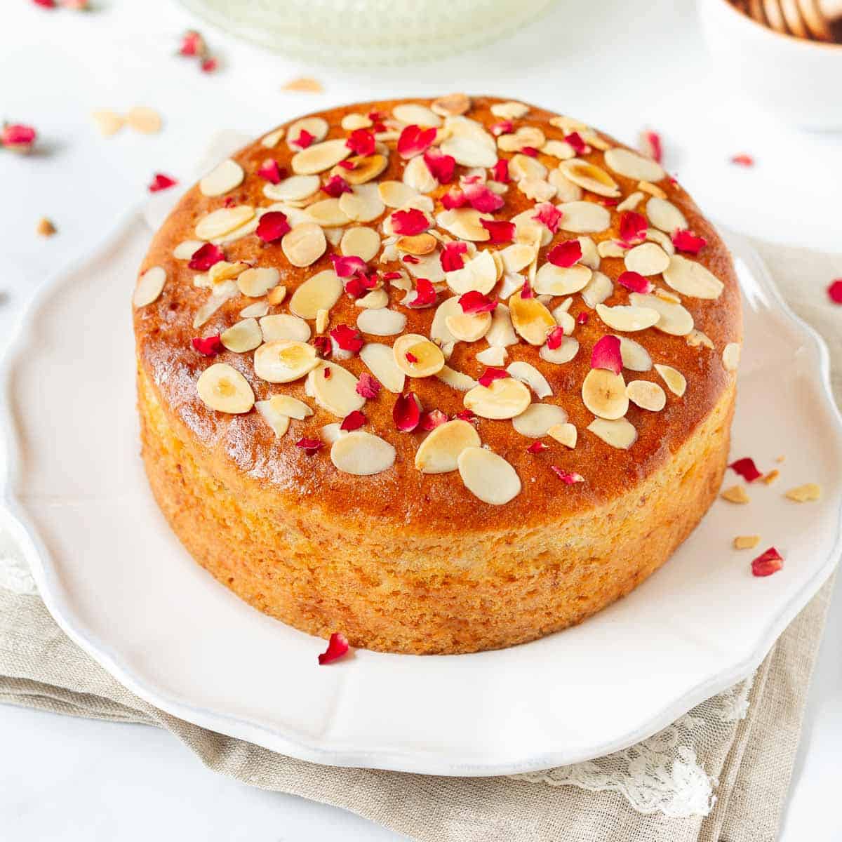 Almond honey cake with rose petals and almonds on top on a platter.