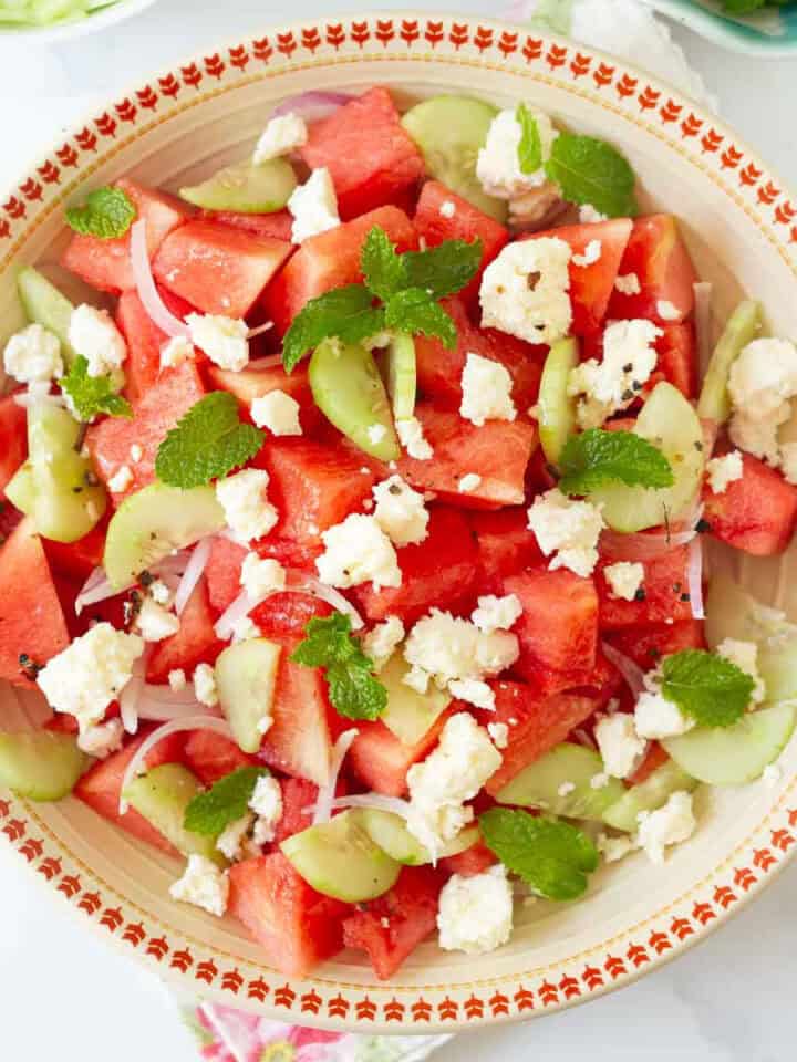A bowl of watermelon salad with onions, cucumbers, mint, and feta cheese.