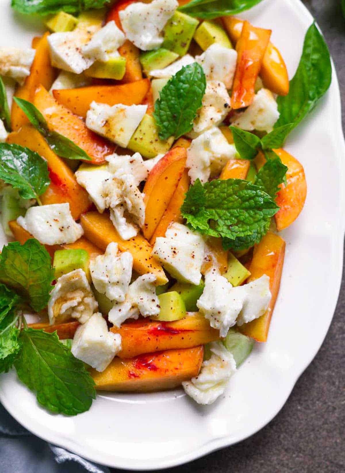 Fresh peach mozzarella salad with mint and basil on a white platter.
