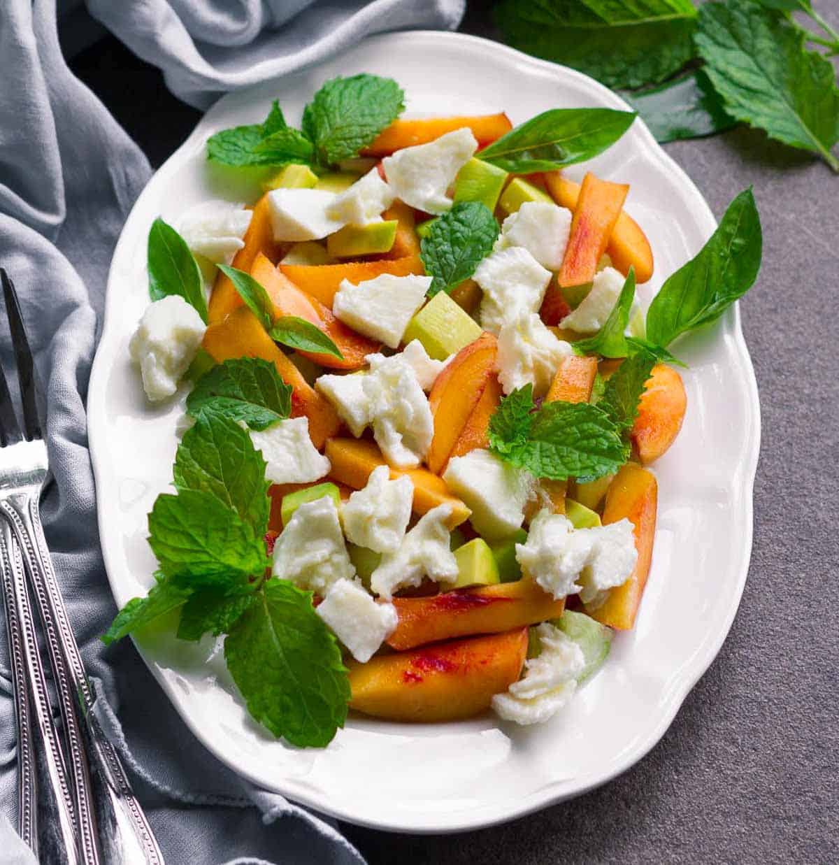 sliced peaches, mozzarella, herbs, and avocado on a plate.
