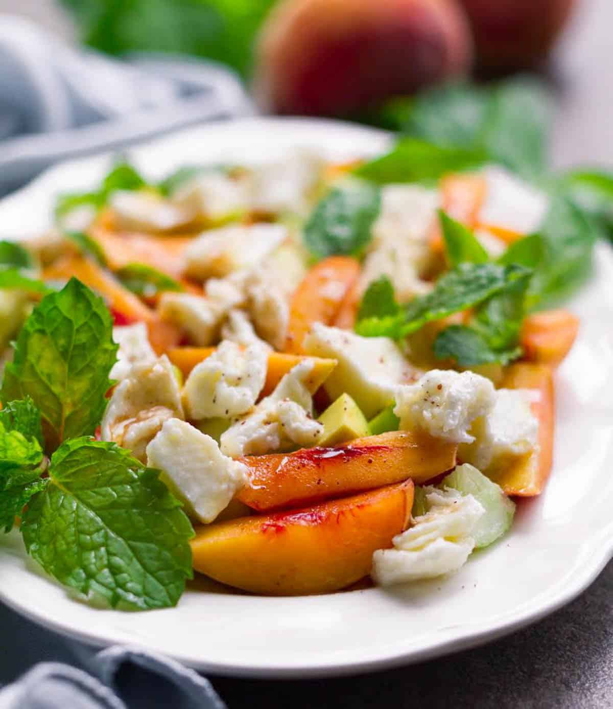 Sliced peaches, mozzarella pieces with herbs on a white plate.